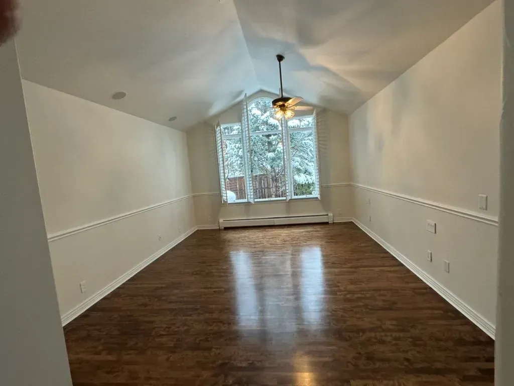 An empty living room with hardwood floors and a ceiling fan.