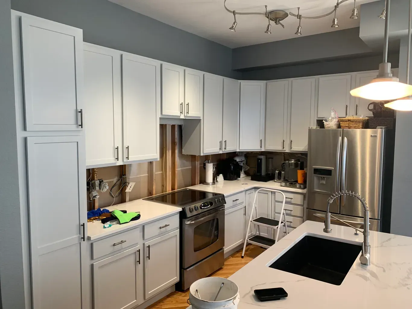 A kitchen with white cabinets , stainless steel appliances , a sink , and a refrigerator.