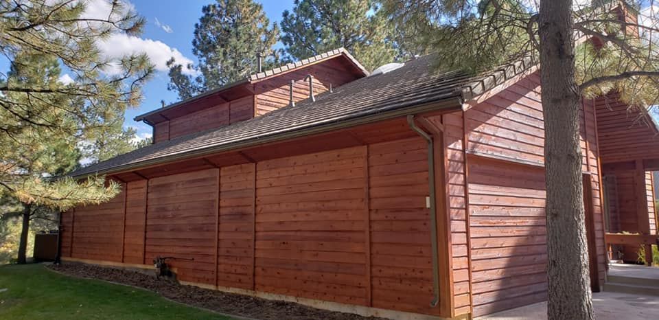 A large wooden building with a roof and trees in the background.