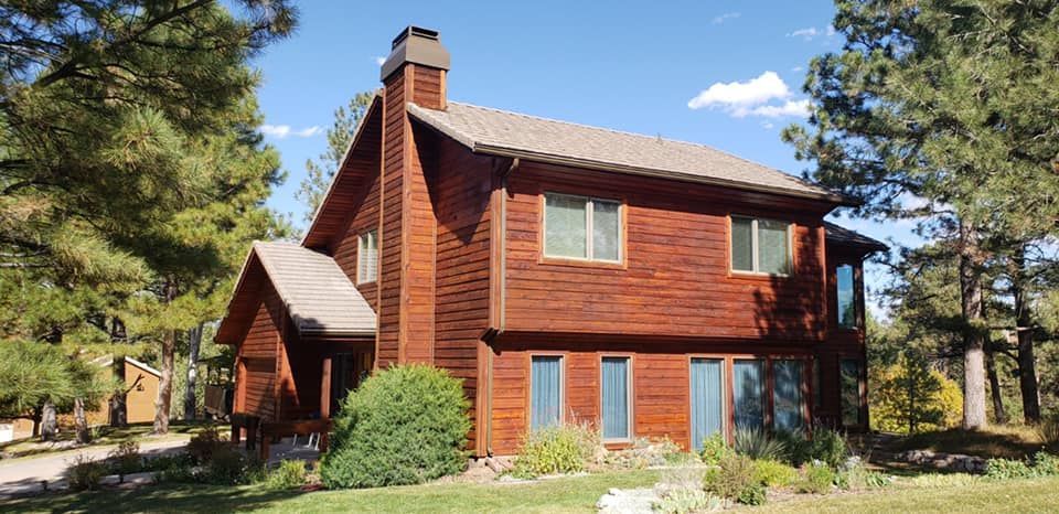 A large wooden house is surrounded by trees on a sunny day.