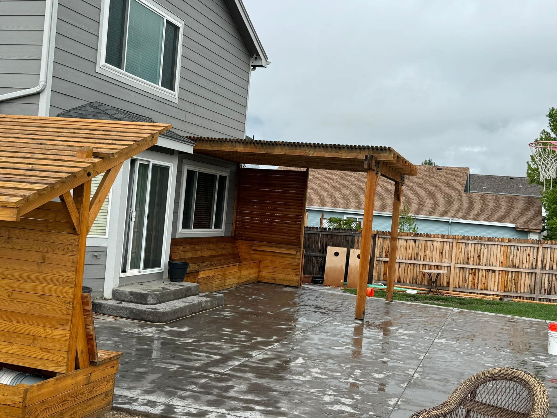 A backyard with a wooden pergola and a wicker chair in the rain.
