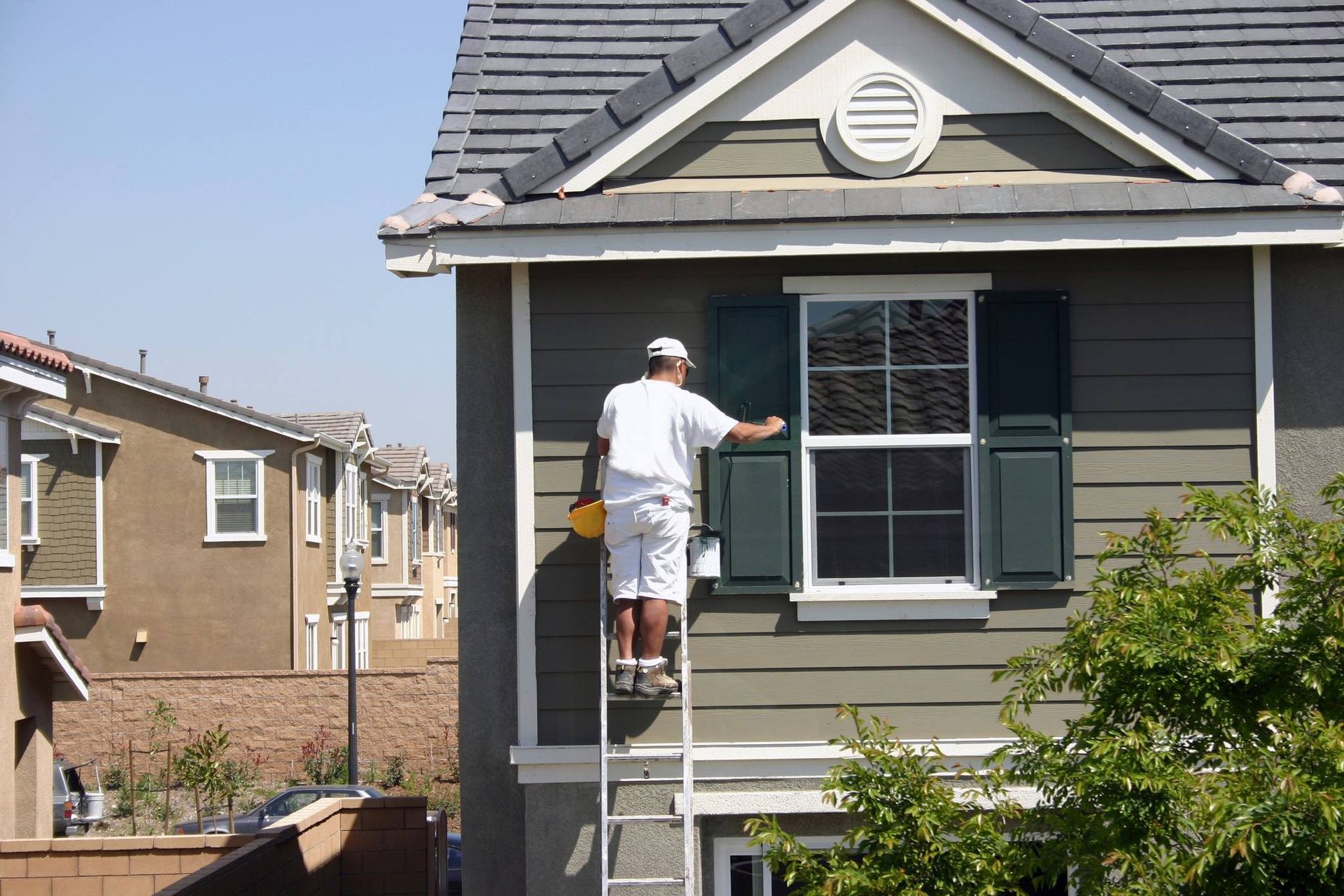 A man is standing on a ladder painting a house.