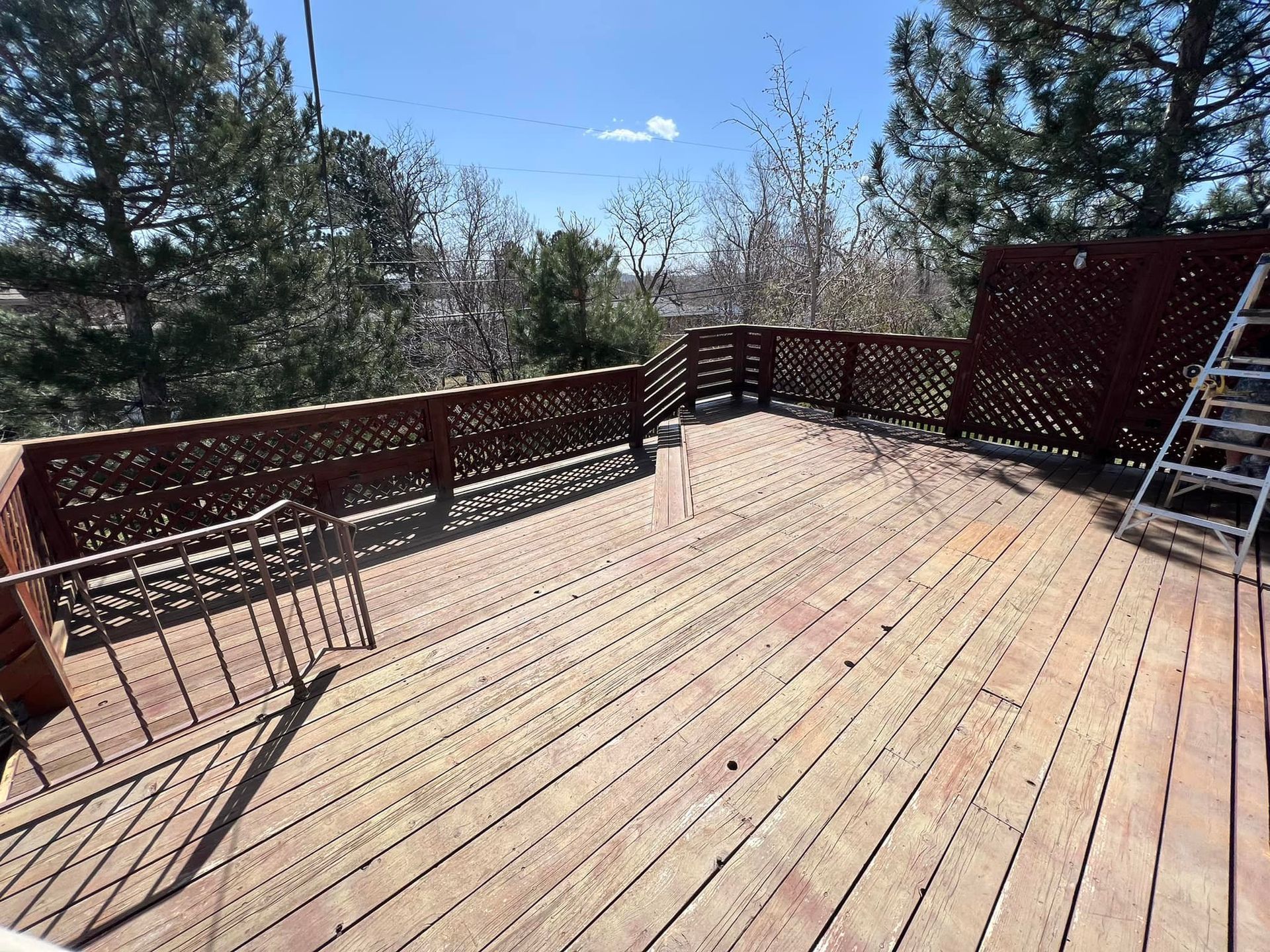 A wooden deck with a ladder on it and trees in the background.