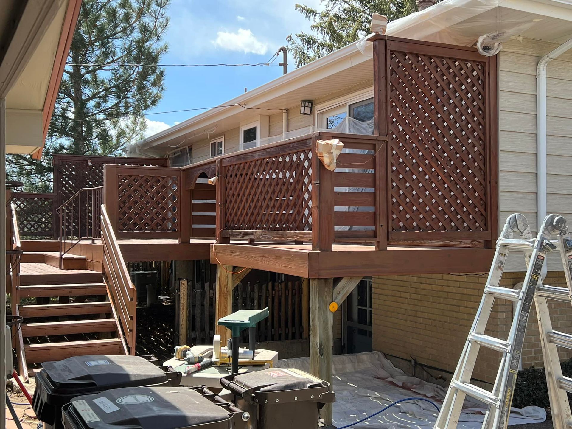 A wooden deck with stairs and a ladder in front of a house.
