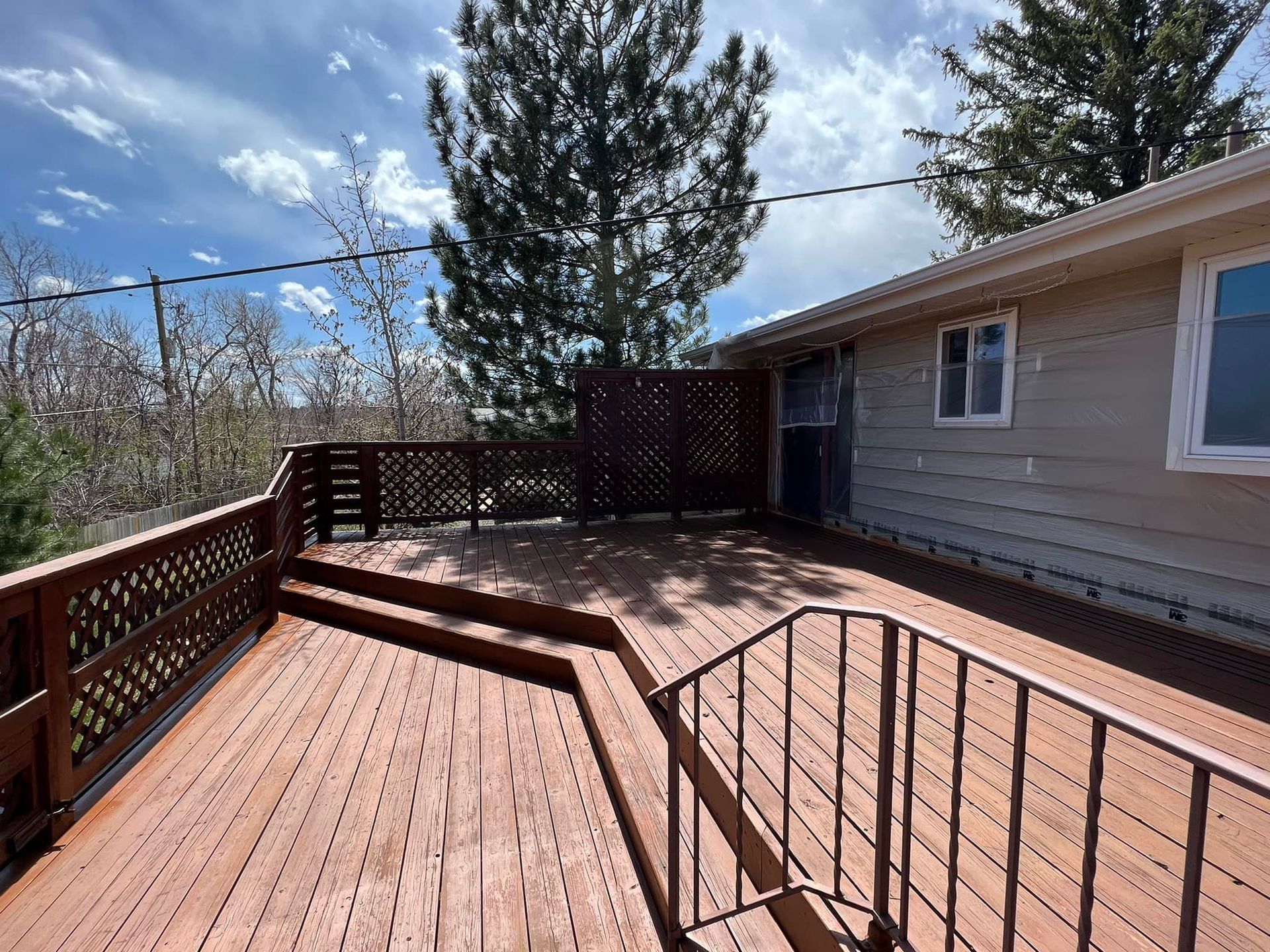 A large wooden deck with stairs leading up to it is in front of a house.