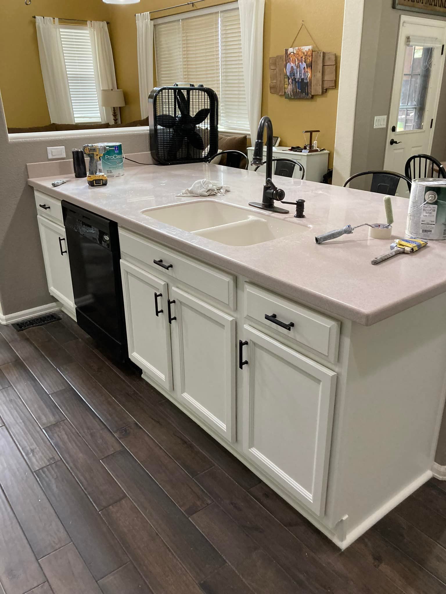 A kitchen with white cabinets , a sink , and a black dishwasher.