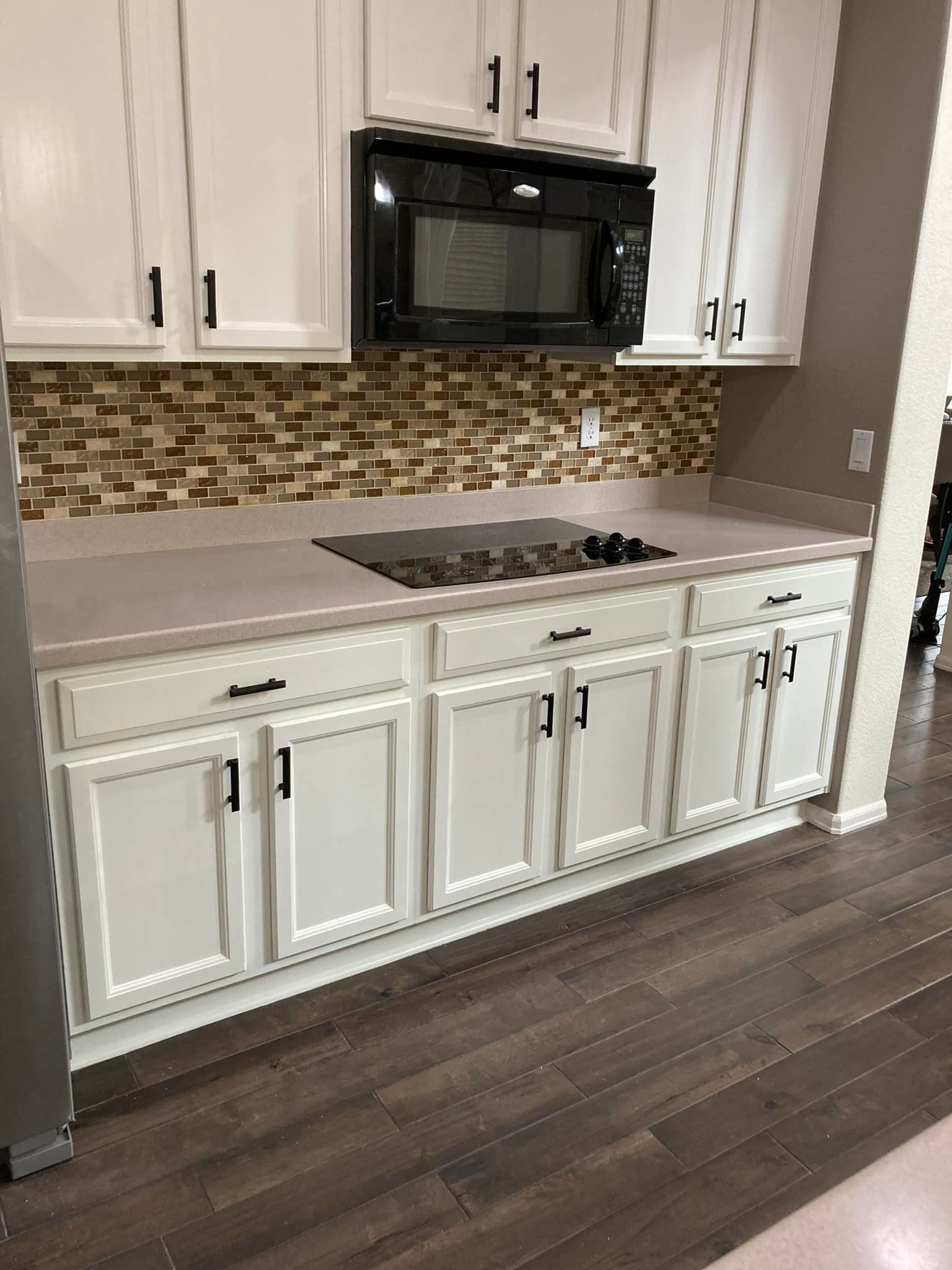 A kitchen with white cabinets , a stove top oven , and a microwave.