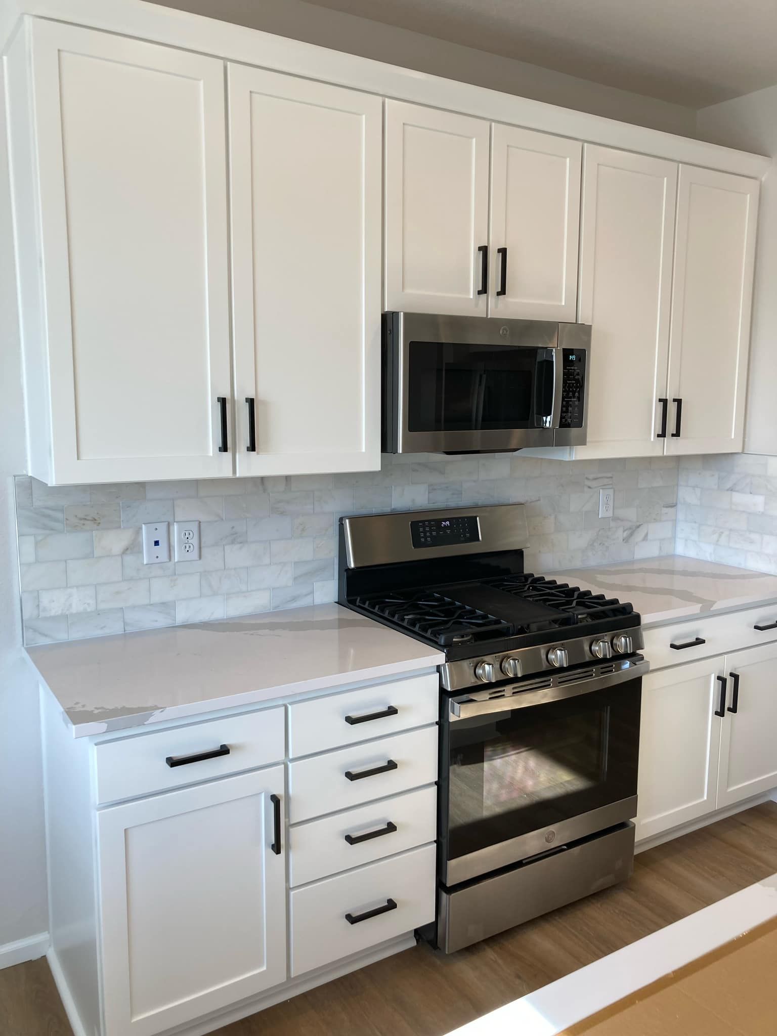 A kitchen with white cabinets , a stove and a microwave.