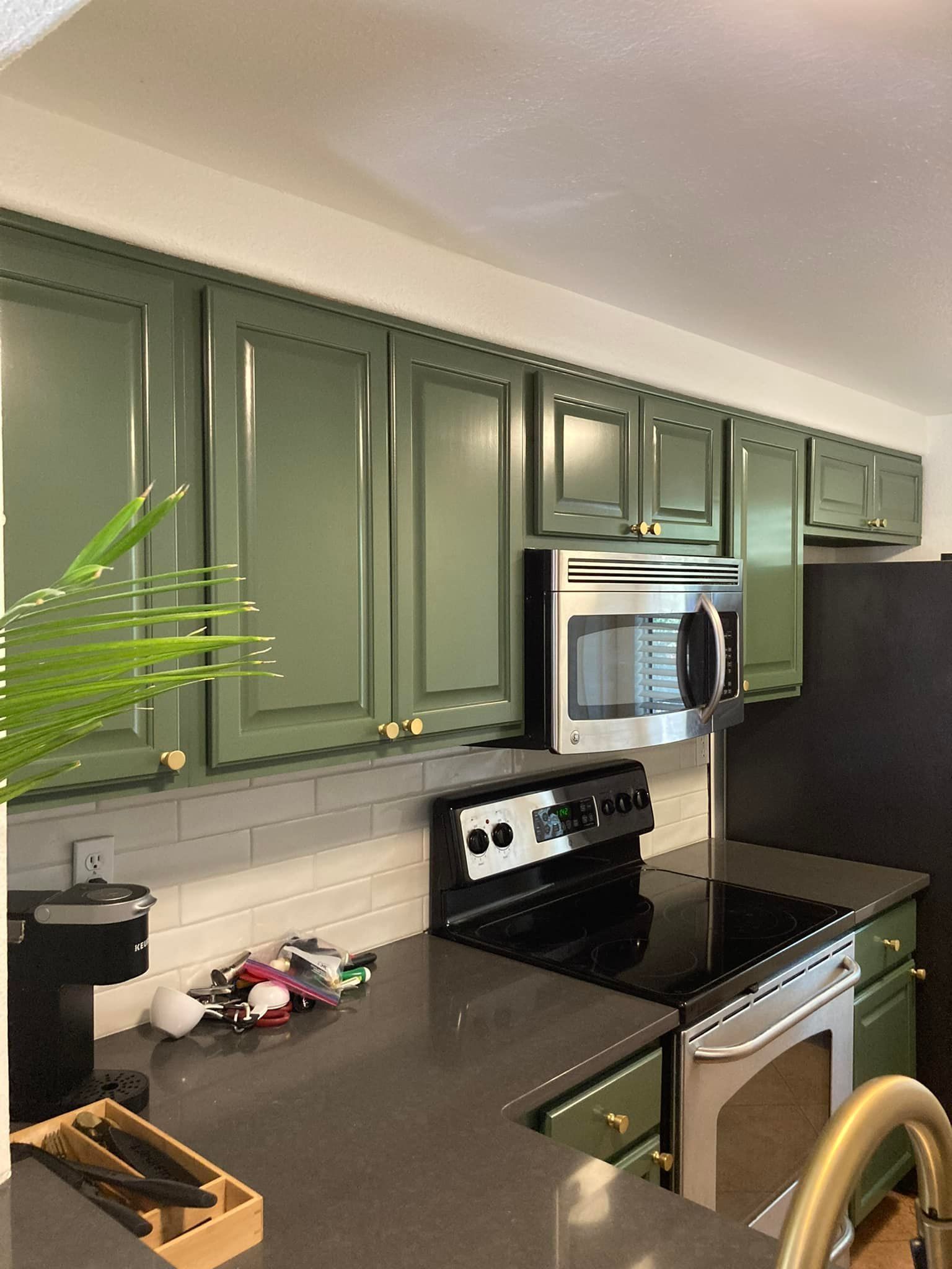 A kitchen with green cabinets , a stove , a microwave , and a sink.