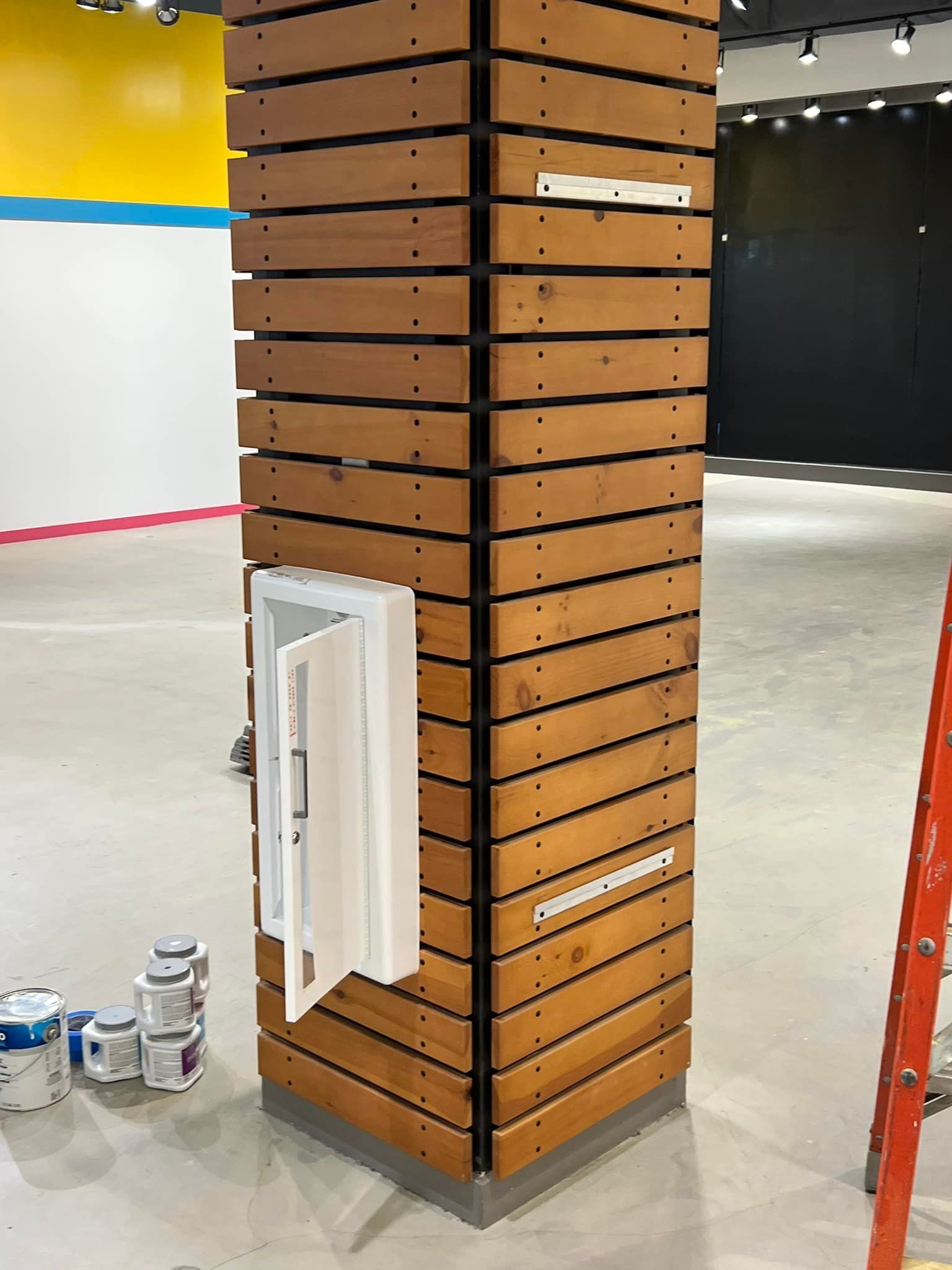 A wooden column in a room with paint cans on the floor