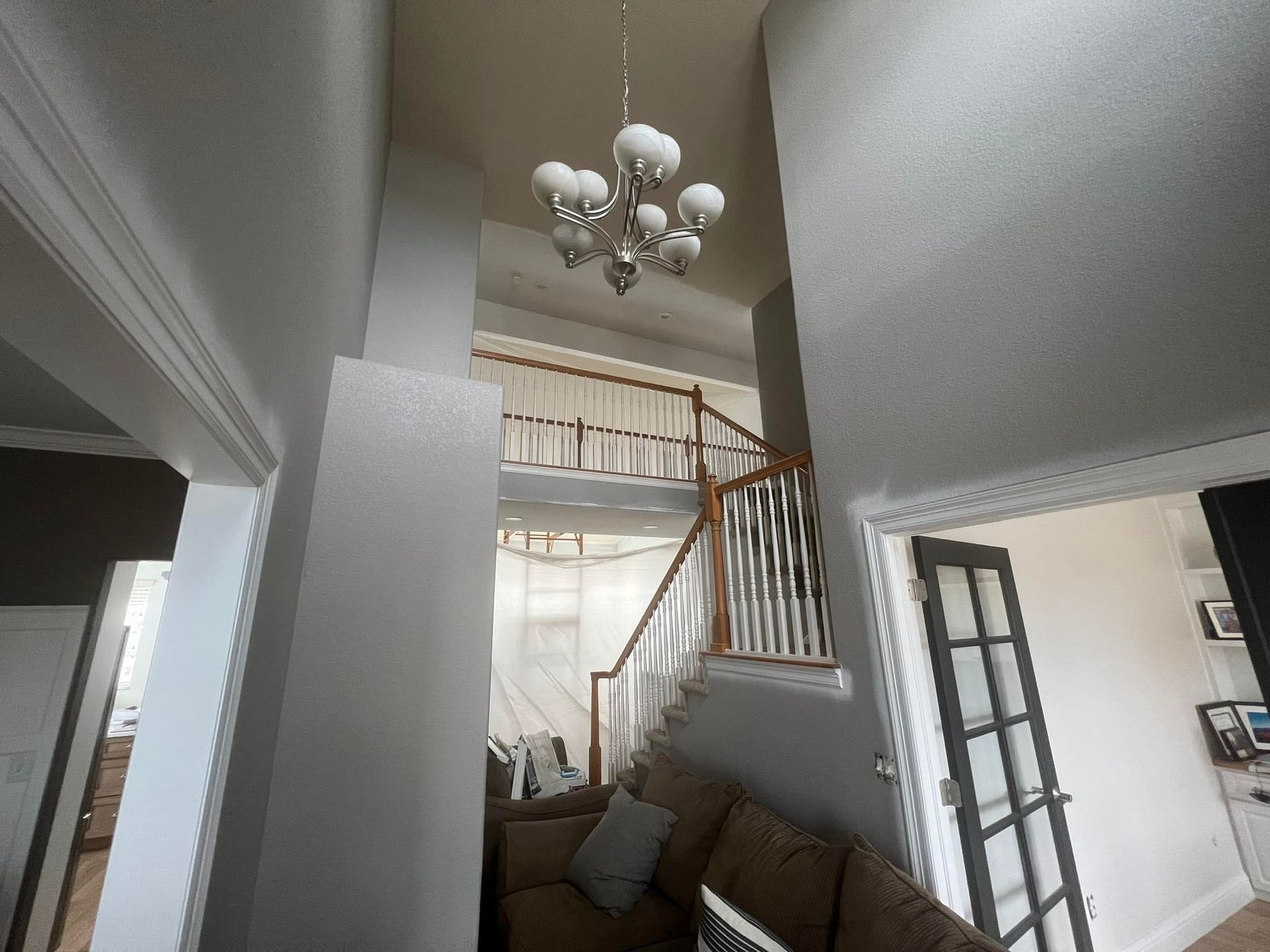 A living room with a couch and stairs and a chandelier hanging from the ceiling.
