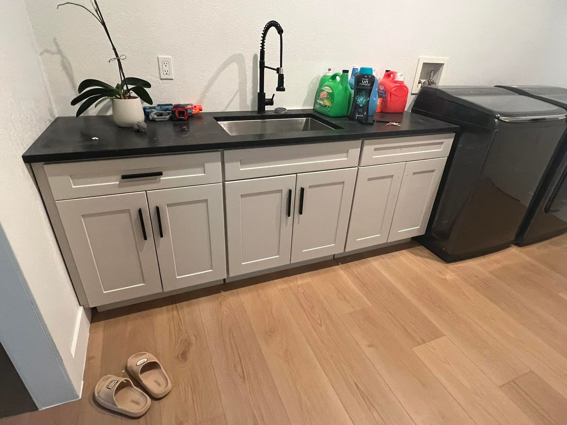 A laundry room with a sink , washing machine , and slippers on the floor.