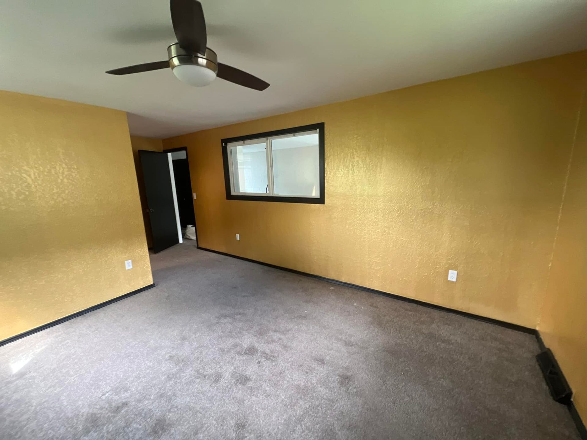 An empty living room with a ceiling fan and a window.