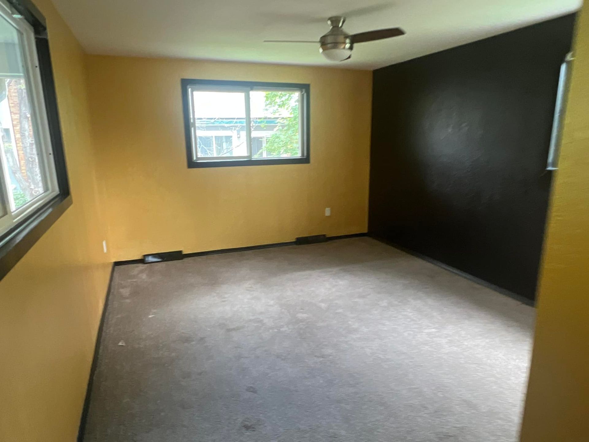 An empty room with a ceiling fan and a window.