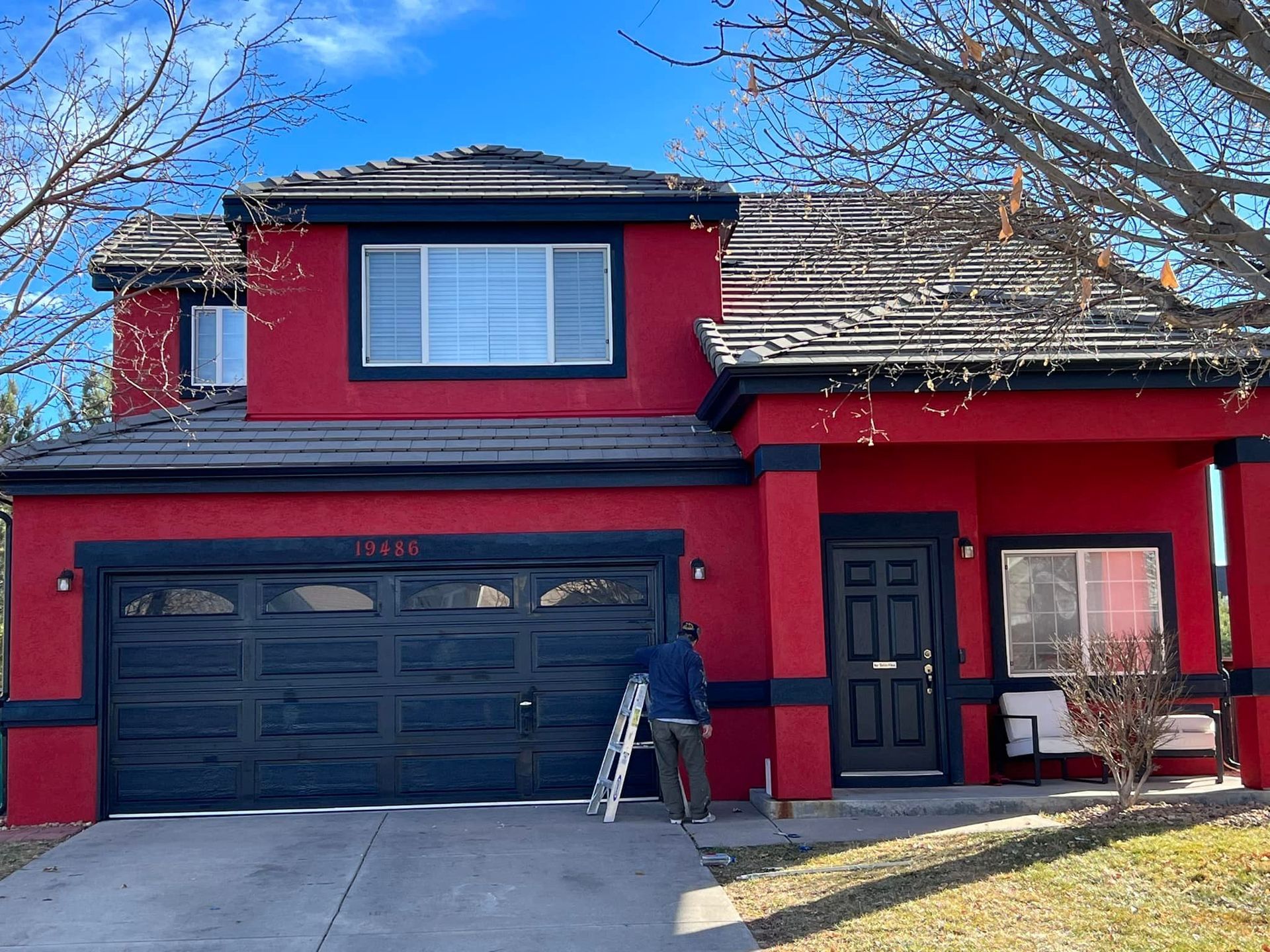 A man is standing on a ladder in front of a red house.