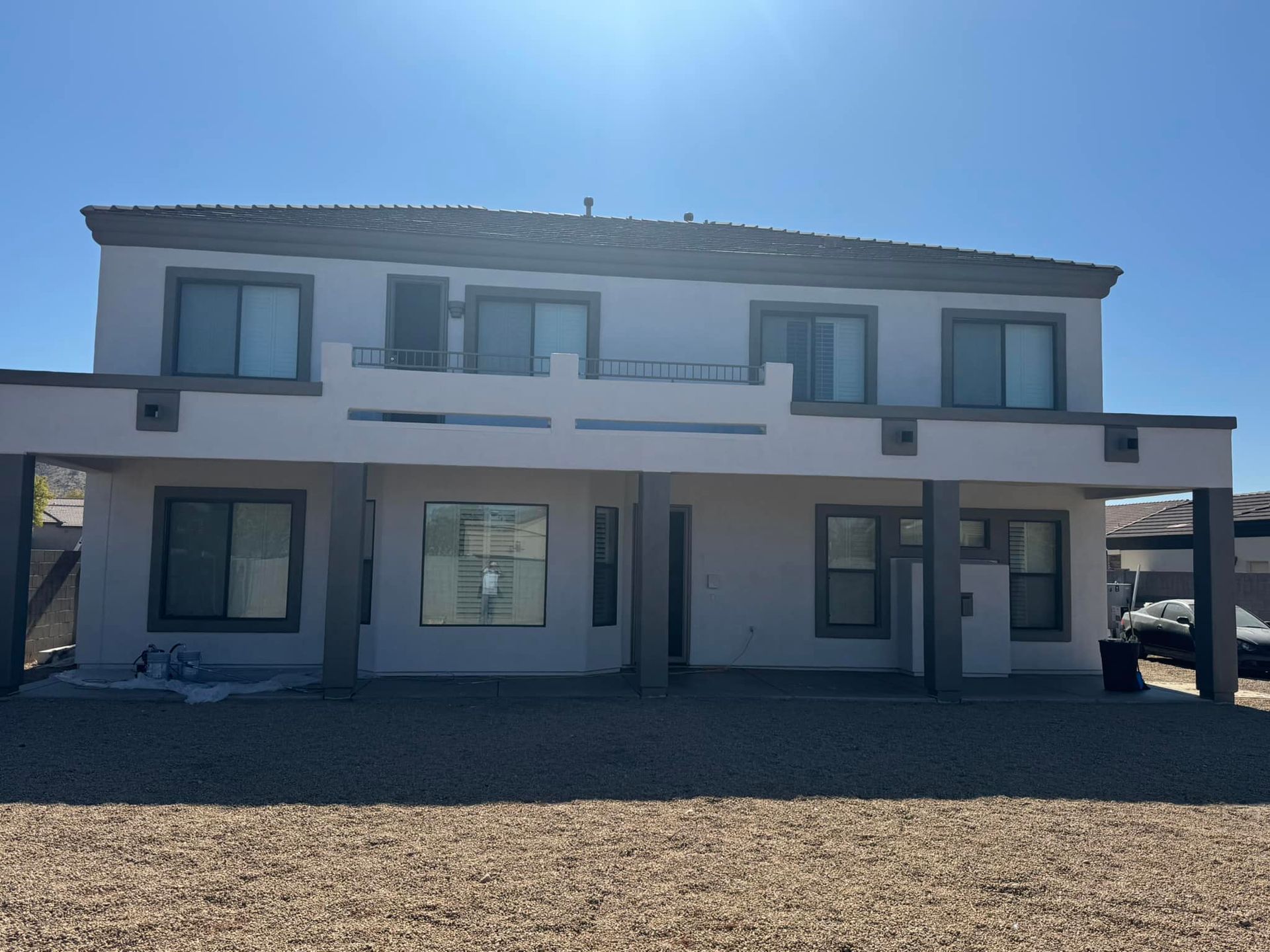 A large white house with a lot of windows is sitting on top of a gravel lot.