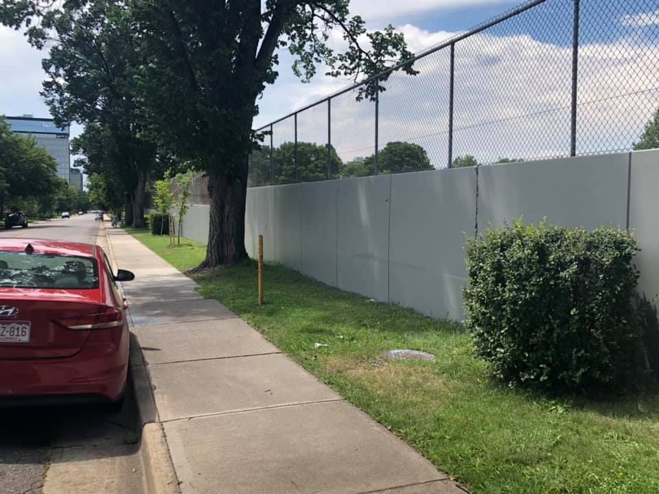 A red car is parked on the side of the road next to a fence.