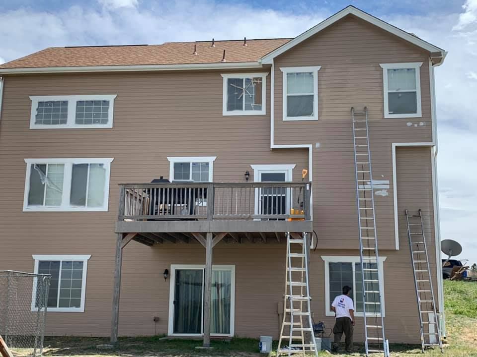 A man is painting the back of a house with a ladder.