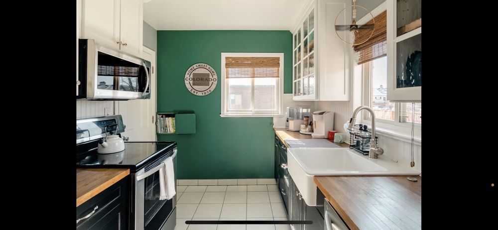 A kitchen with green walls , white cabinets , stainless steel appliances , a sink and a microwave.