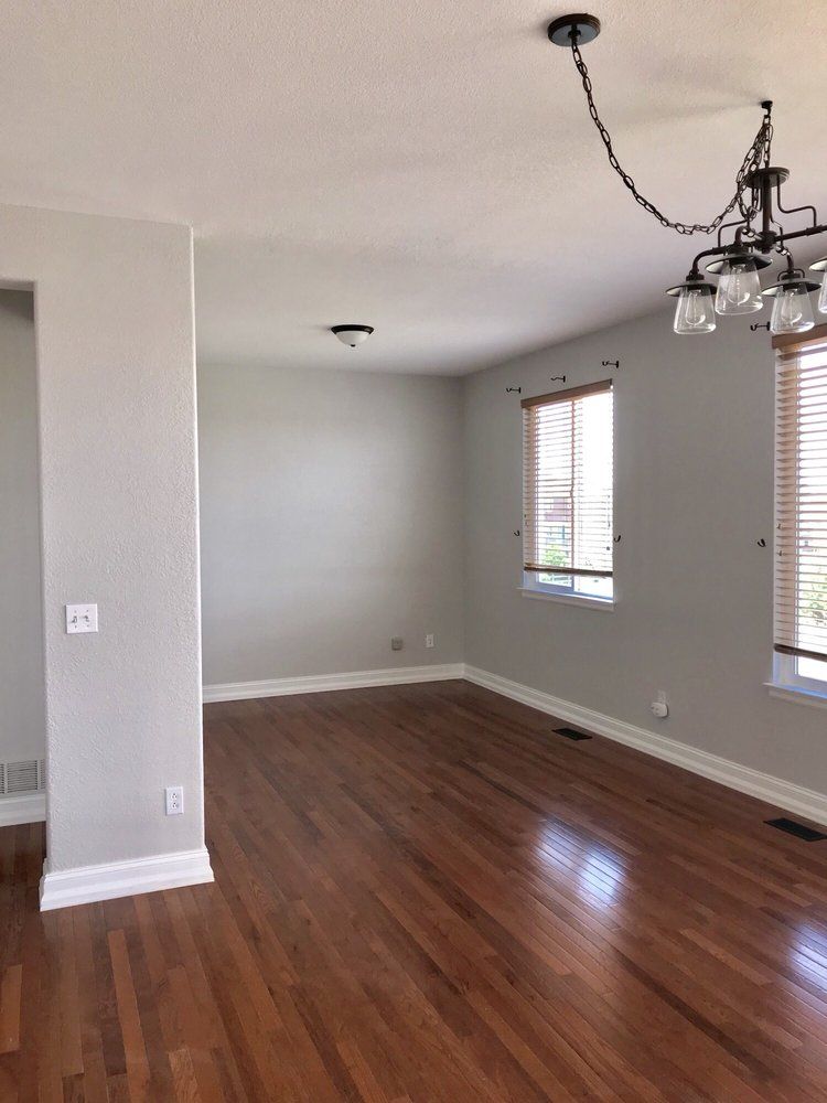 An empty living room with hardwood floors and a chandelier hanging from the ceiling.