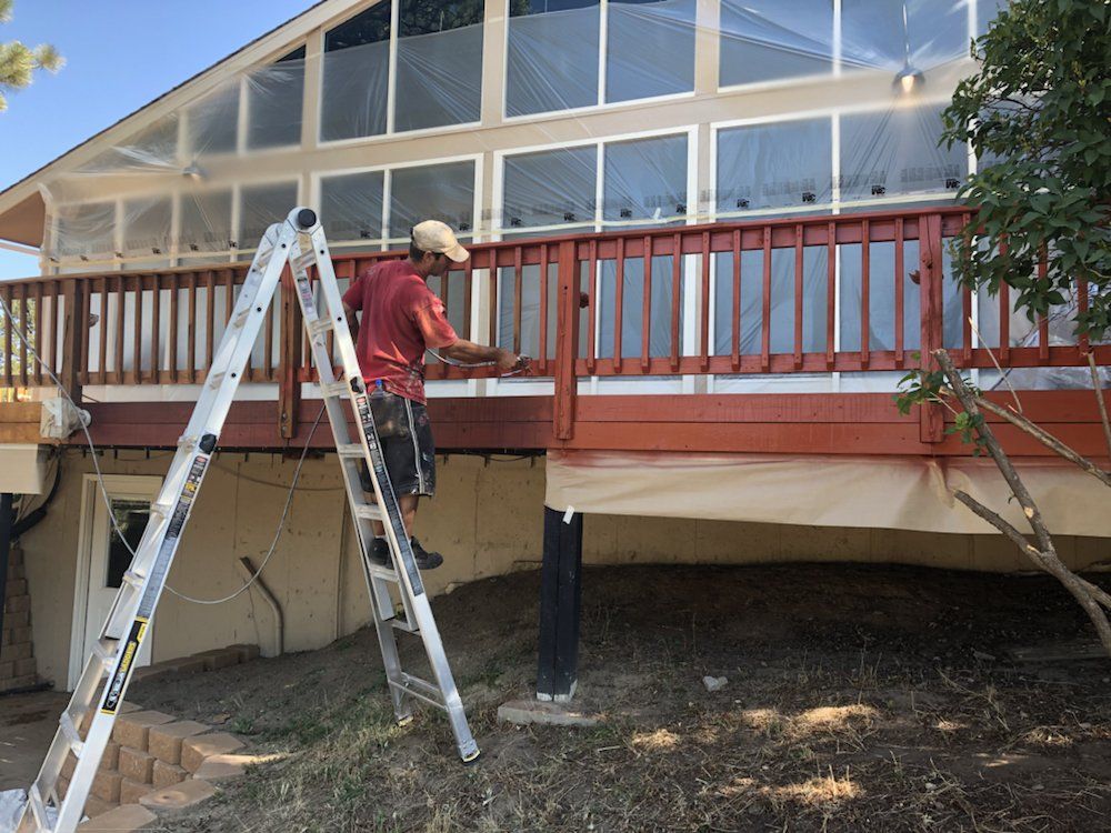 A man is standing on a ladder painting a deck.