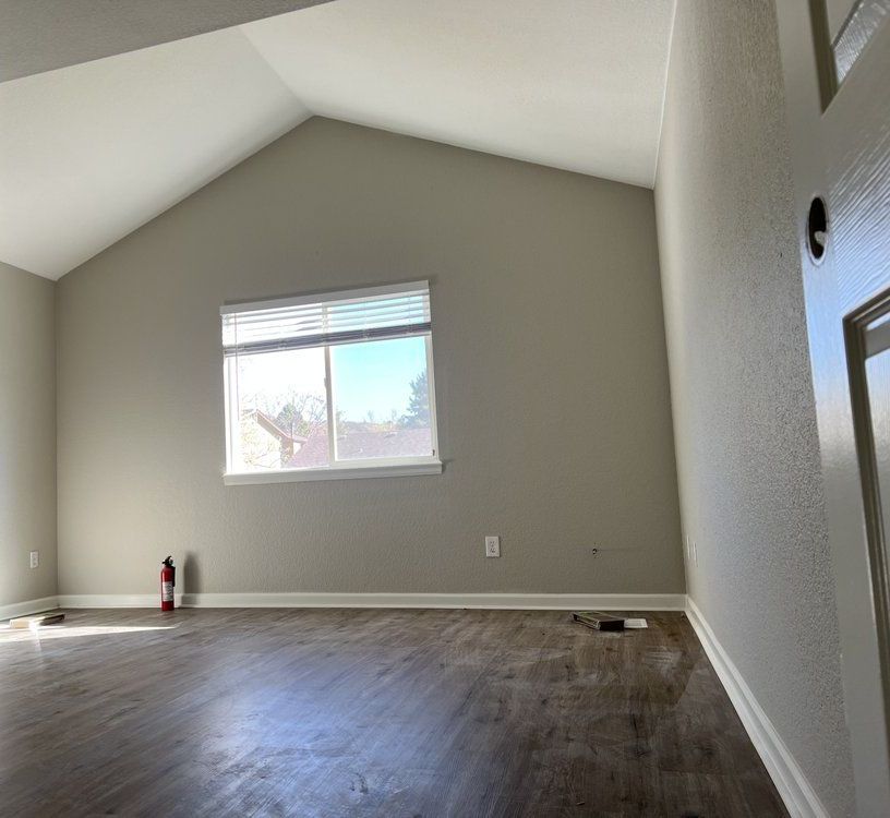 An empty living room with a vaulted ceiling and a large window.