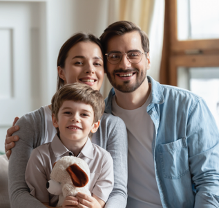 Family of three smiling at the camera, posing indoors; a child holds a stuffed animal.