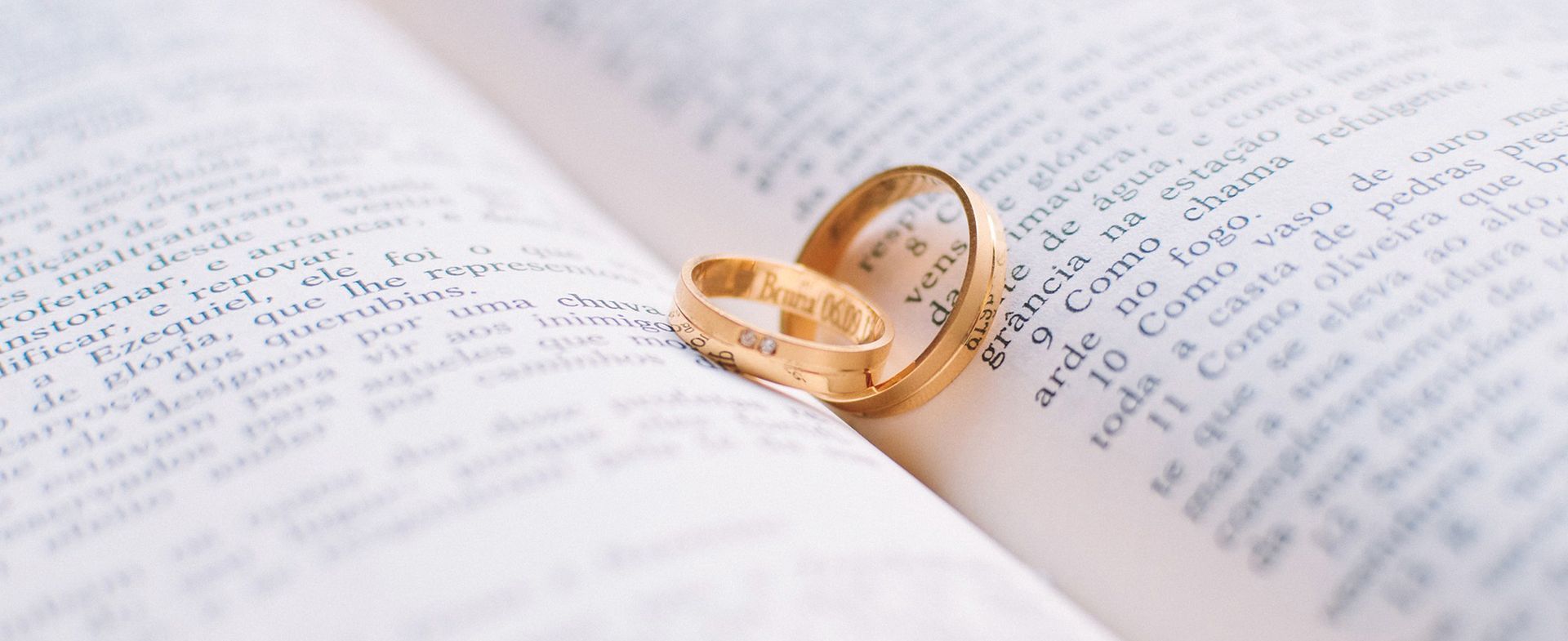 Two gold wedding rings on an open book, emphasizing marriage and commitment.