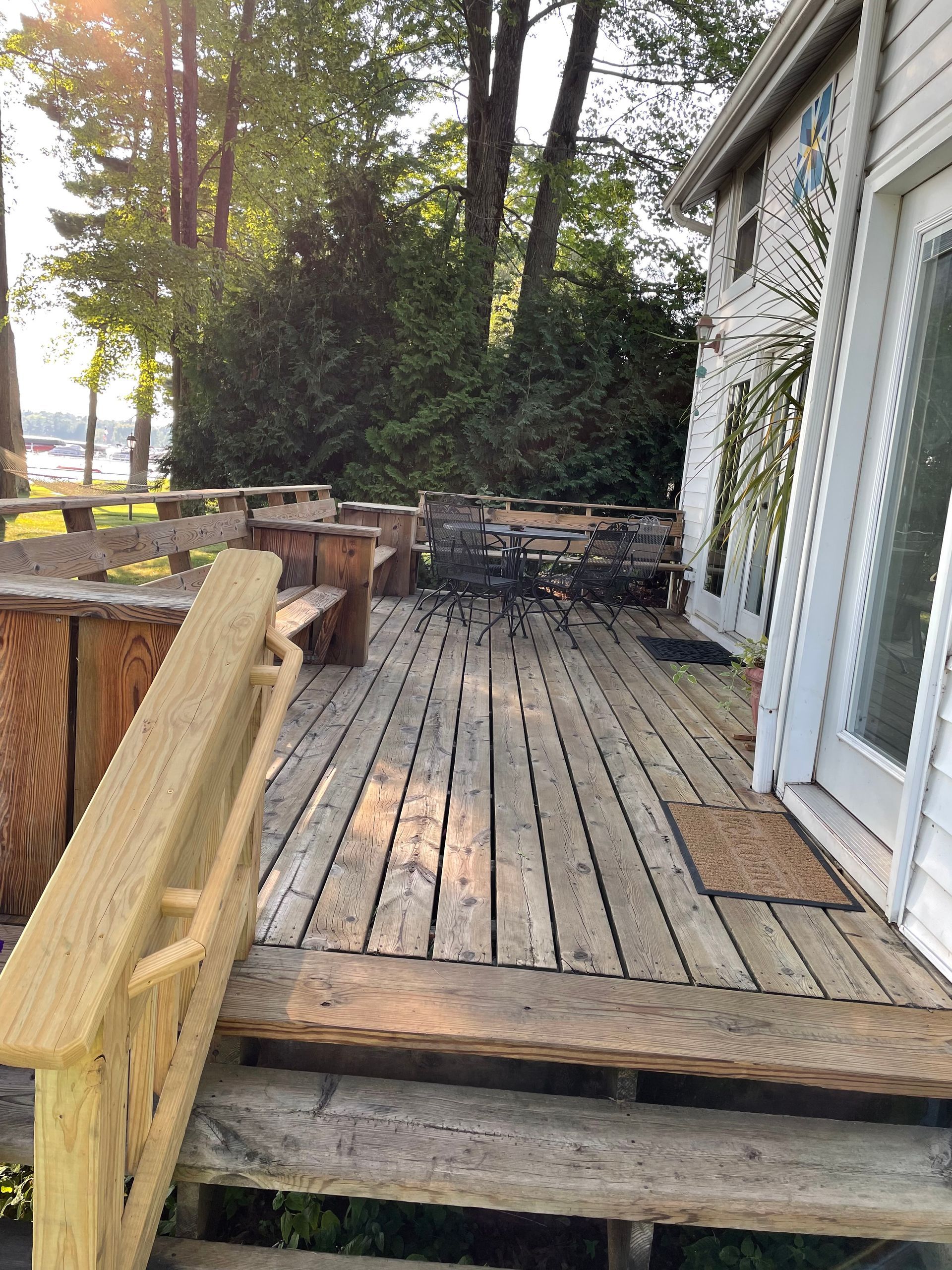 A wooden deck with stairs leading up to it and a white house in the background.
