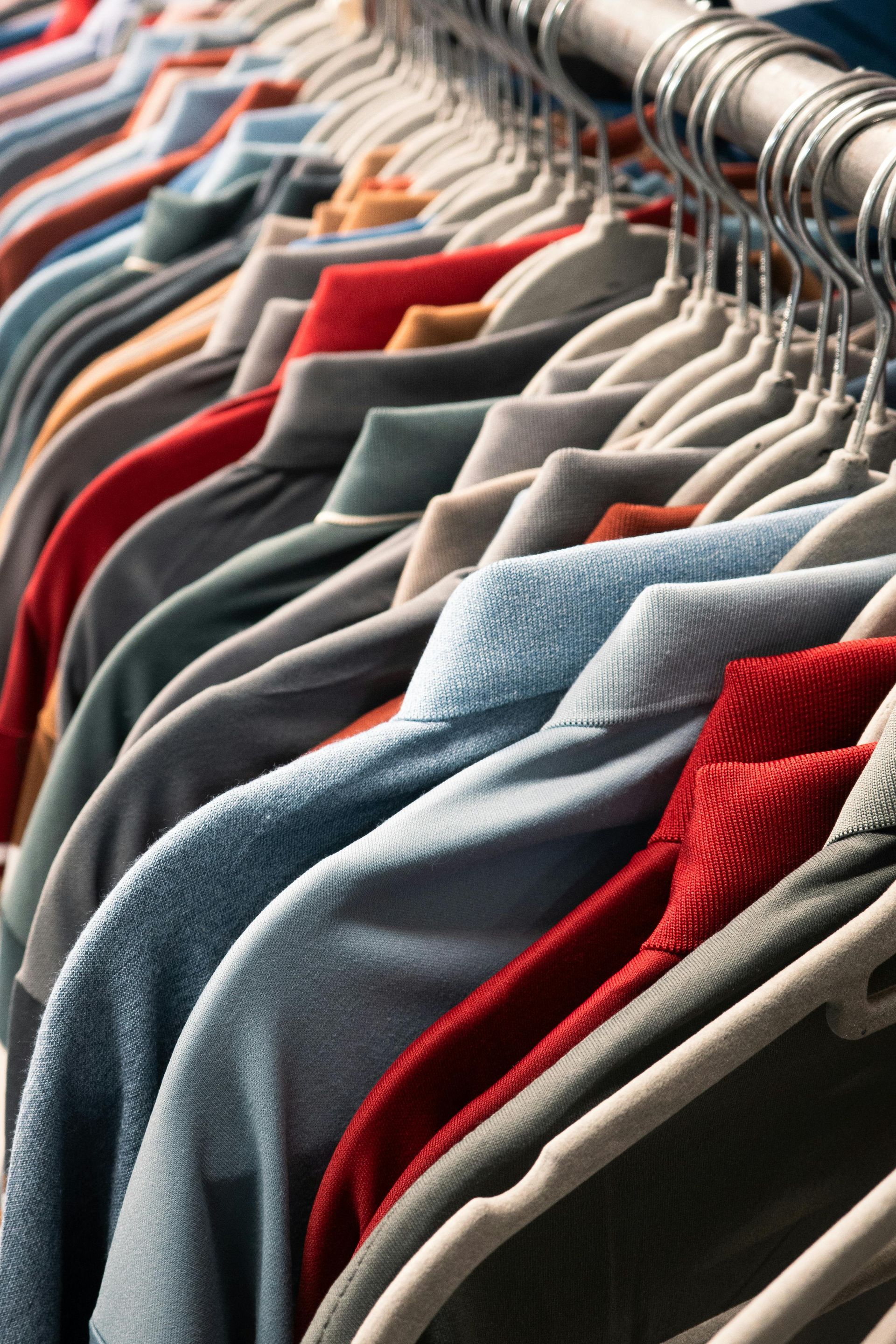 A rack of shirts in various colors and textures, hanging closely together on hangers.