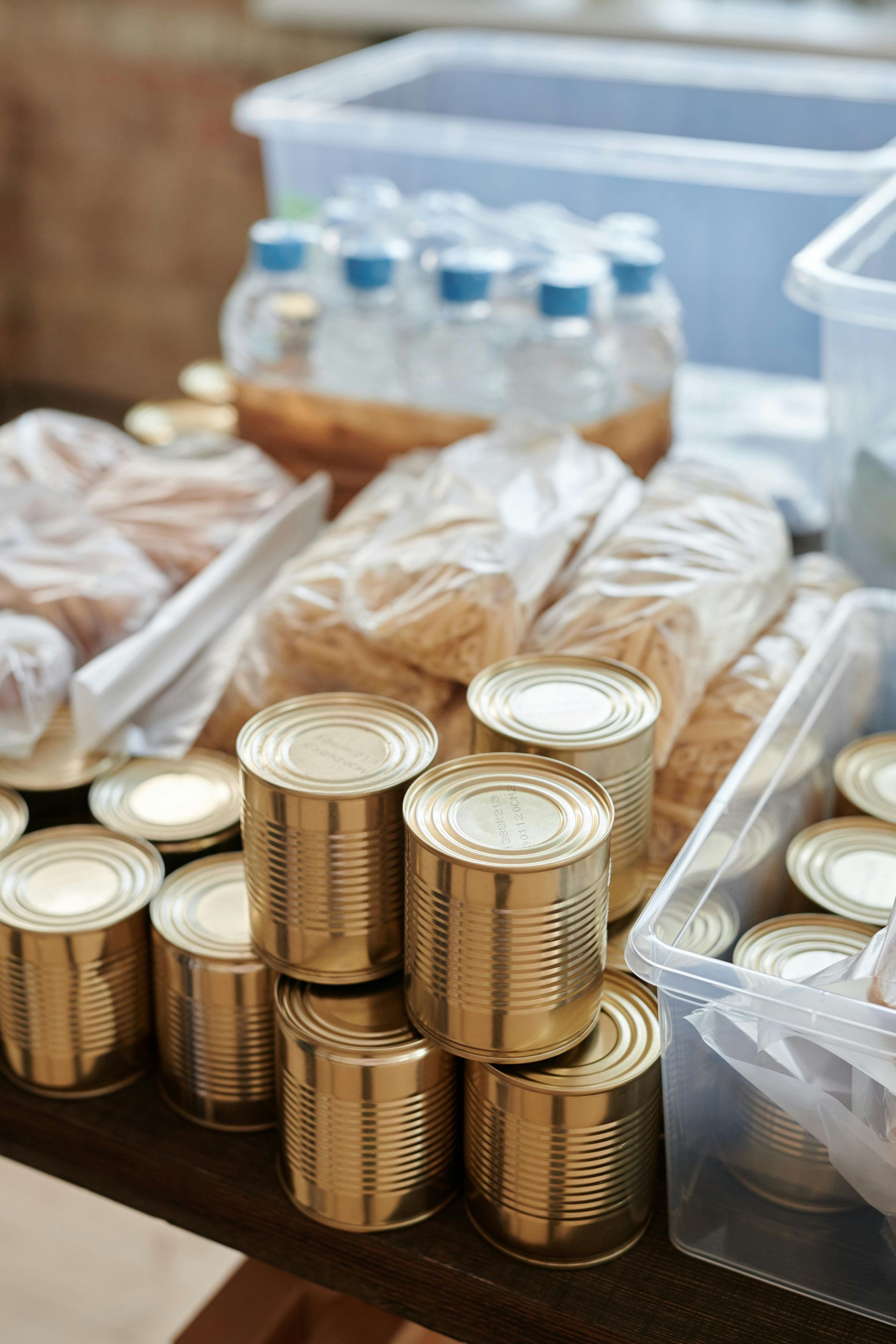 A collection of food donations, including canned goods, bags of dry food, and plastic water bottles, on a wooden table.