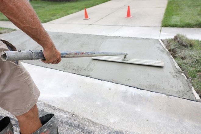 Person smoothing fresh concrete with a trowel on a driveway.