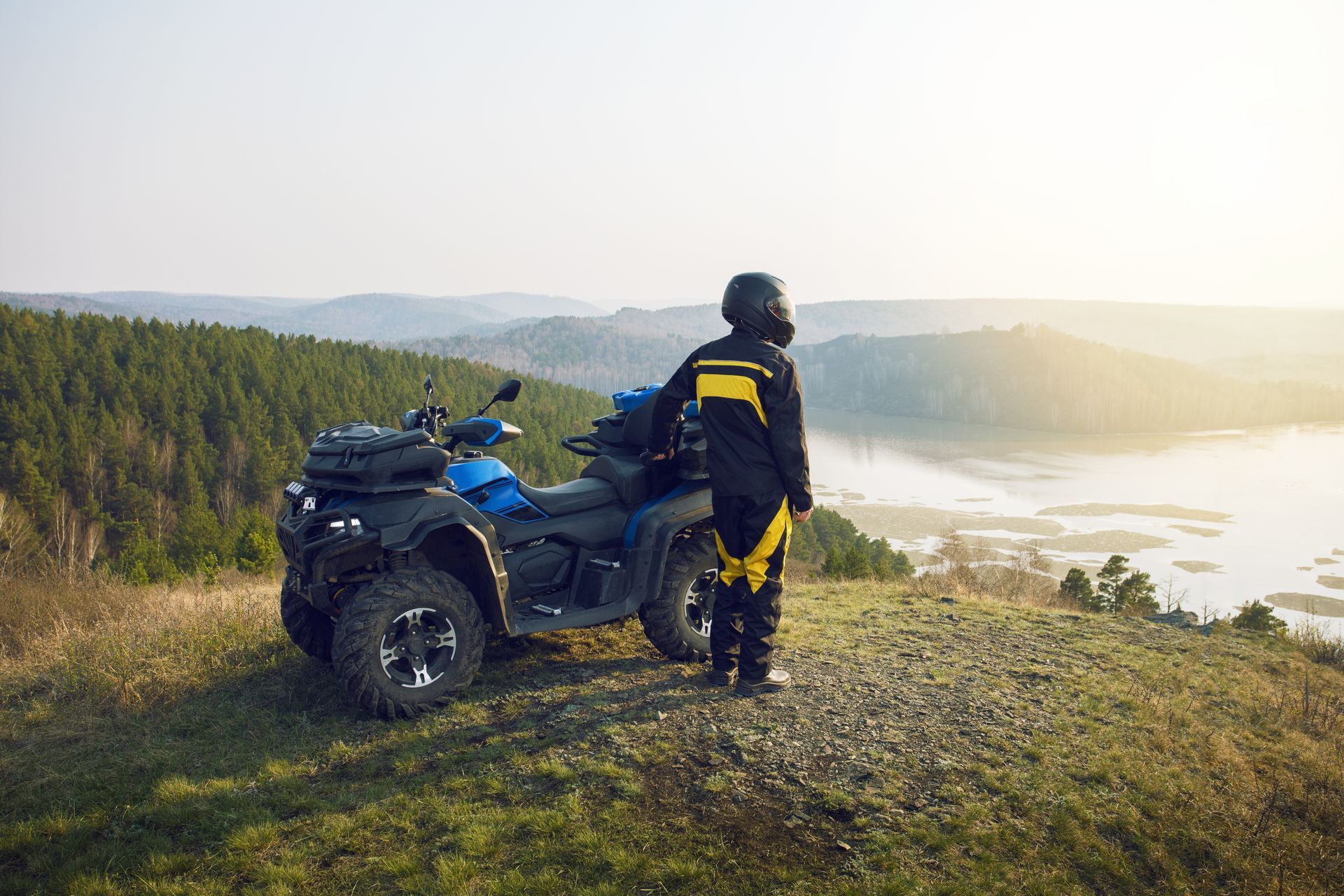 A man is standing next to an atv on top of a hill.
