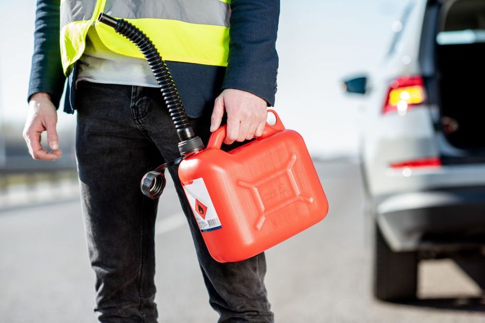 A man is holding a gas can on the side of the road.