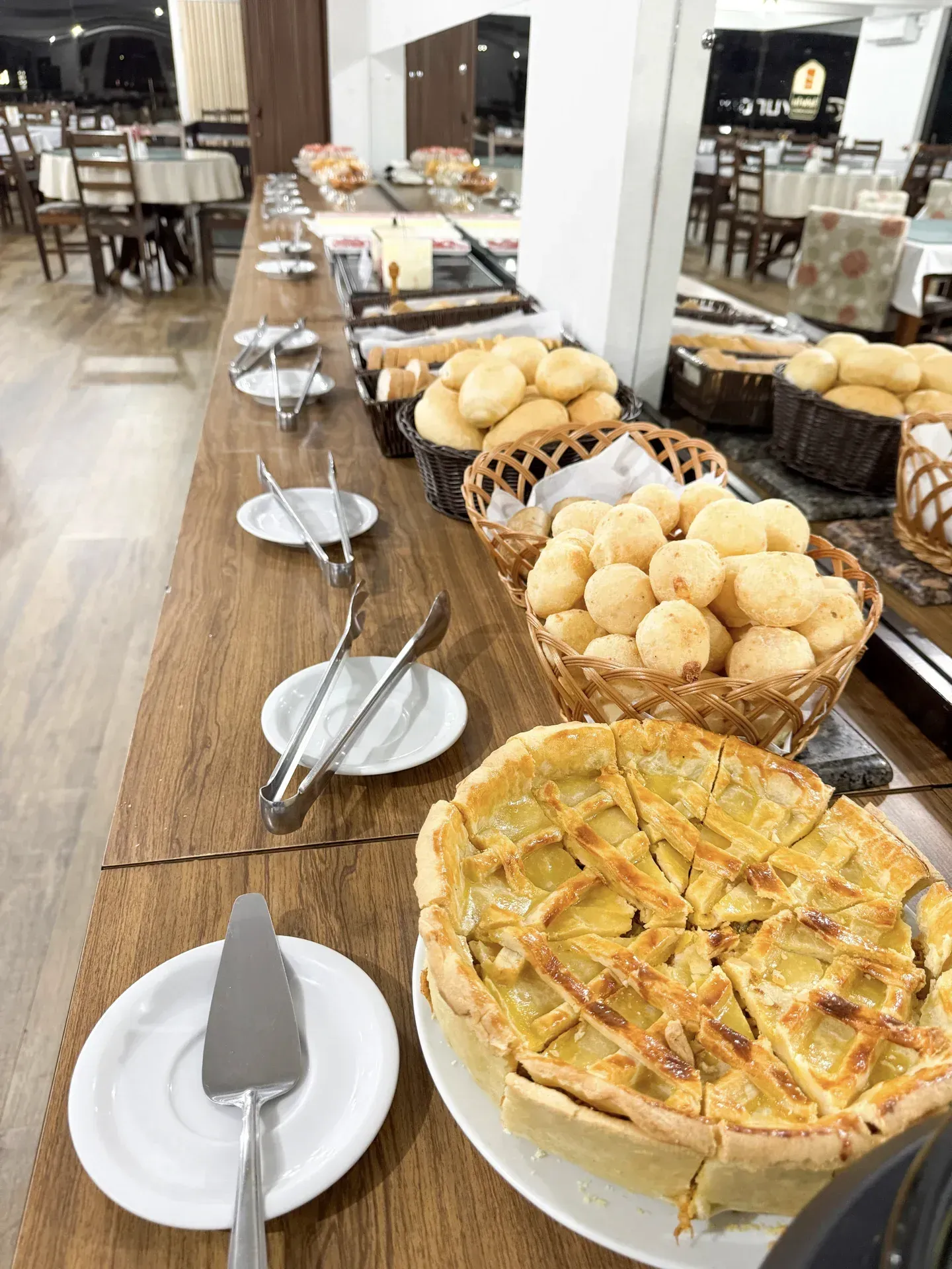 Mesa de bufê com diversos pães, doces e uma torta em um ambiente de restaurante.