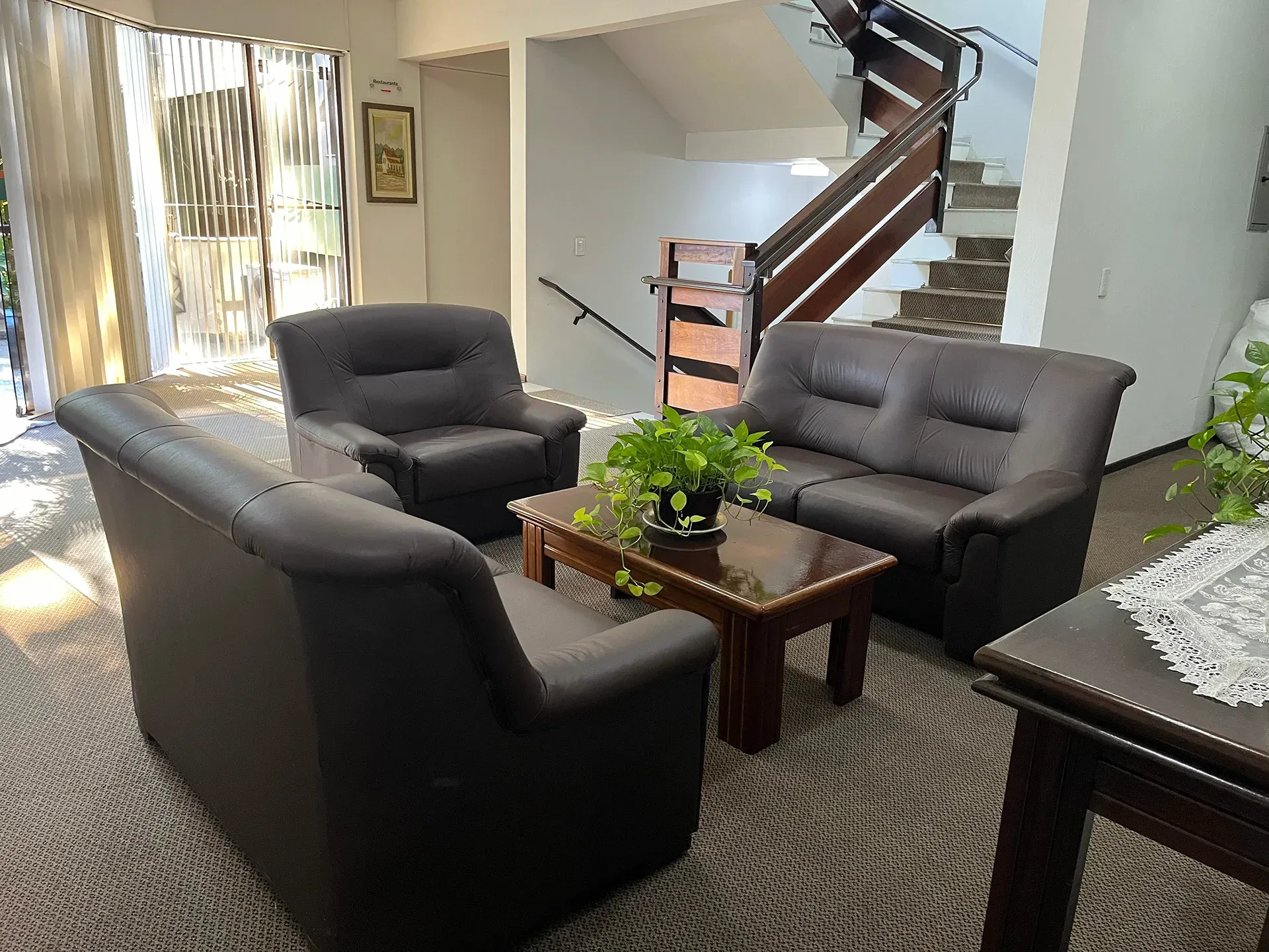 Uma área de estar com sofás marrons, uma mesa de centro com uma planta e uma escada ao fundo.