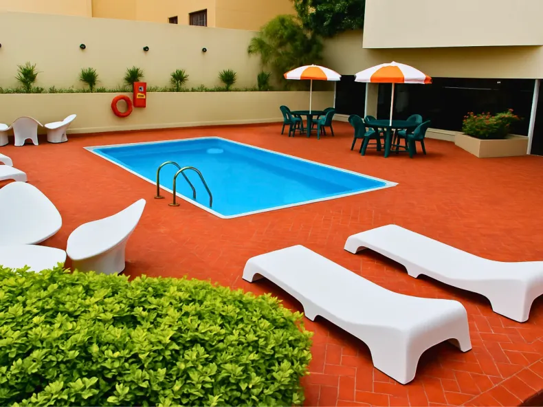 Piscina com espreguiçadeiras, mesas e guarda-sóis em um pátio de tijolos vermelhos.