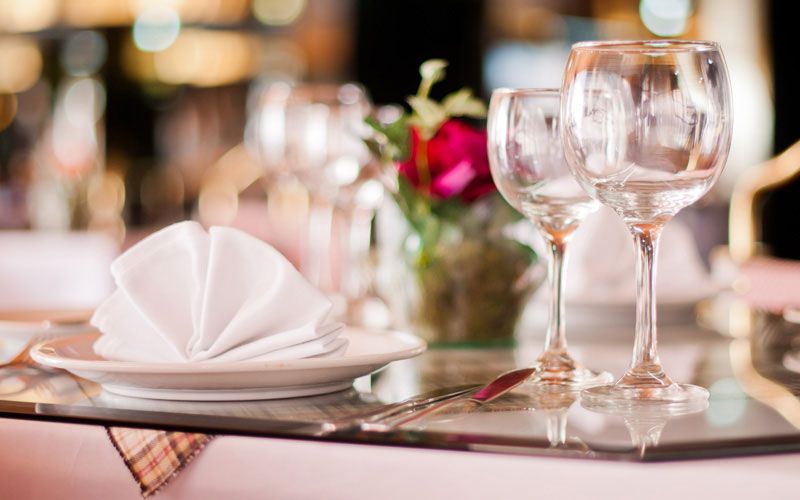 Pátio externo do hotel com mesas, cadeiras e uma pérgola de madeira, com vista para uma pequena piscina e um prédio.