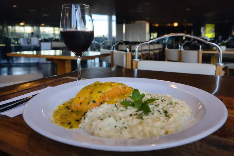 Salmão com molho e risoto, servido com vinho tinto em um ambiente de restaurante.