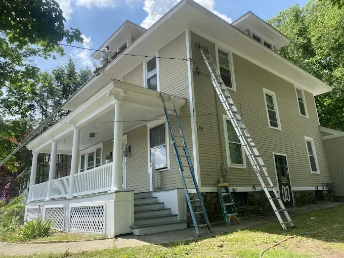 A two-story house with two ladders propped against it. House is painted light green with white trim.