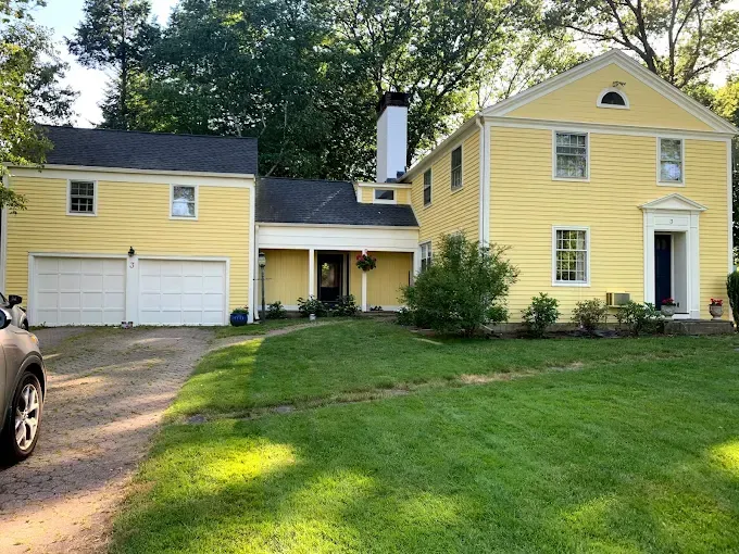 Yellow colonial house with white garage doors and a green lawn.