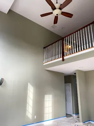High-ceilinged living room with olive green walls, a balcony, and a brown ceiling fan.