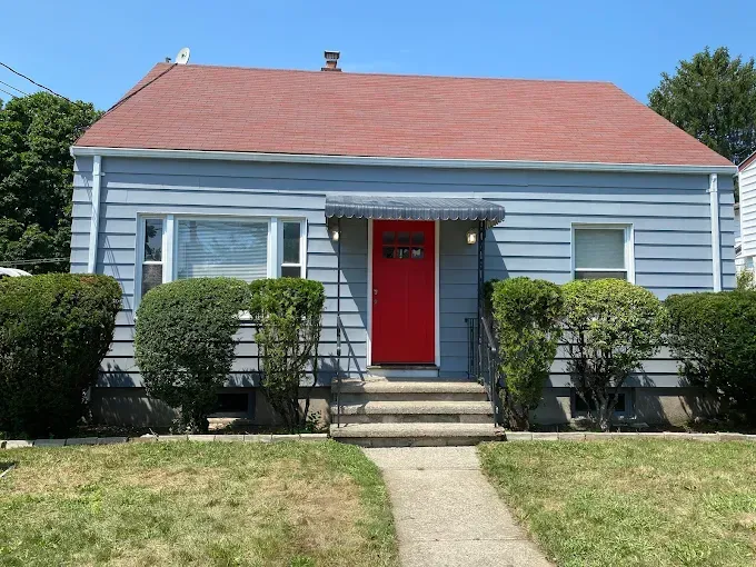 Blue house with a red door and red roof, with a walkway leading up to it.