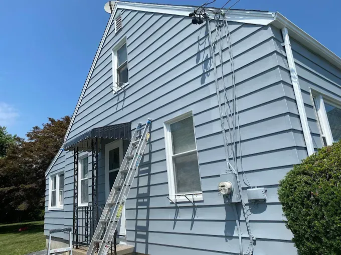 Light blue house with ladder, electrical wires, and awning.