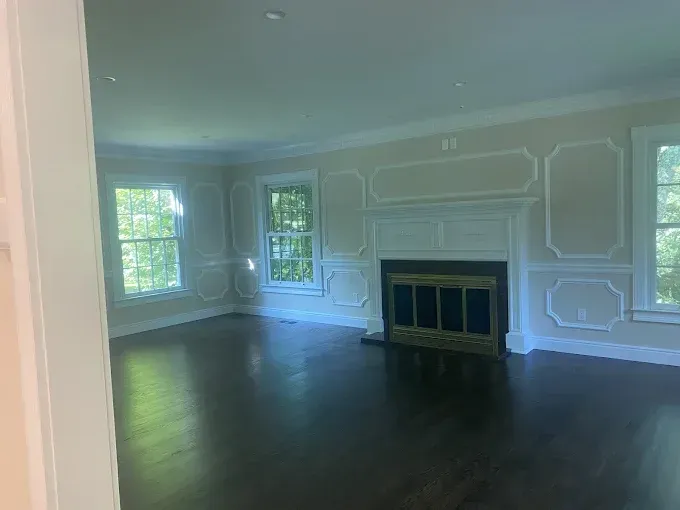 Empty living room with dark wood floor, fireplace, and beige walls with white trim.