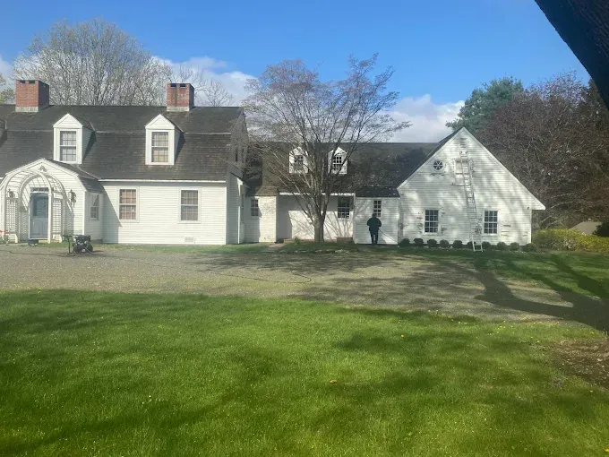 White colonial house with a grassy yard and small trees under a blue sky.