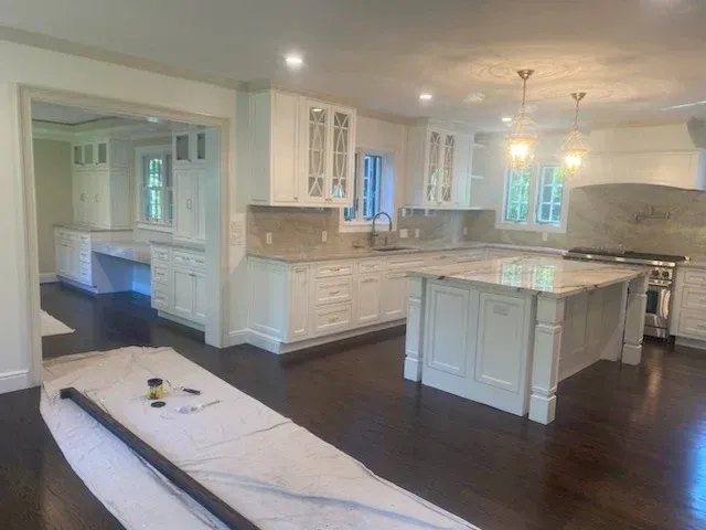 Spacious white kitchen with dark wood floors, granite countertops, and island.
