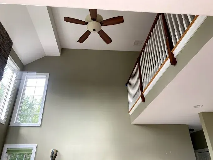 Interior view of a two-story room with a staircase and ceiling fan; green walls, white trim and wood railing.