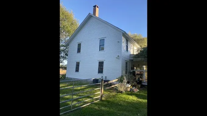 White two-story house with a wooden fence and chimney under a clear blue sky.