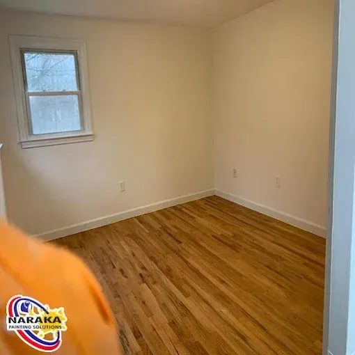 Empty room with hardwood floors, white walls, and a window.